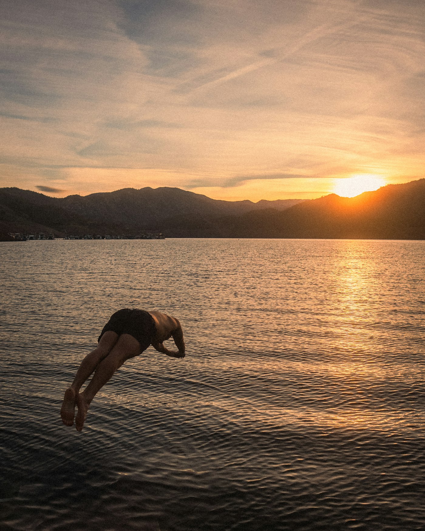 Silhouette of a person diving head first into a lake at sunset