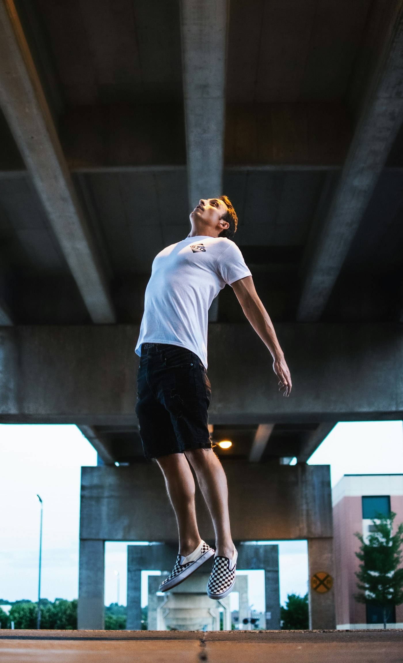 Man in a white T-shirt pushing off the ground under a concrete bridge, the take-off of a jump