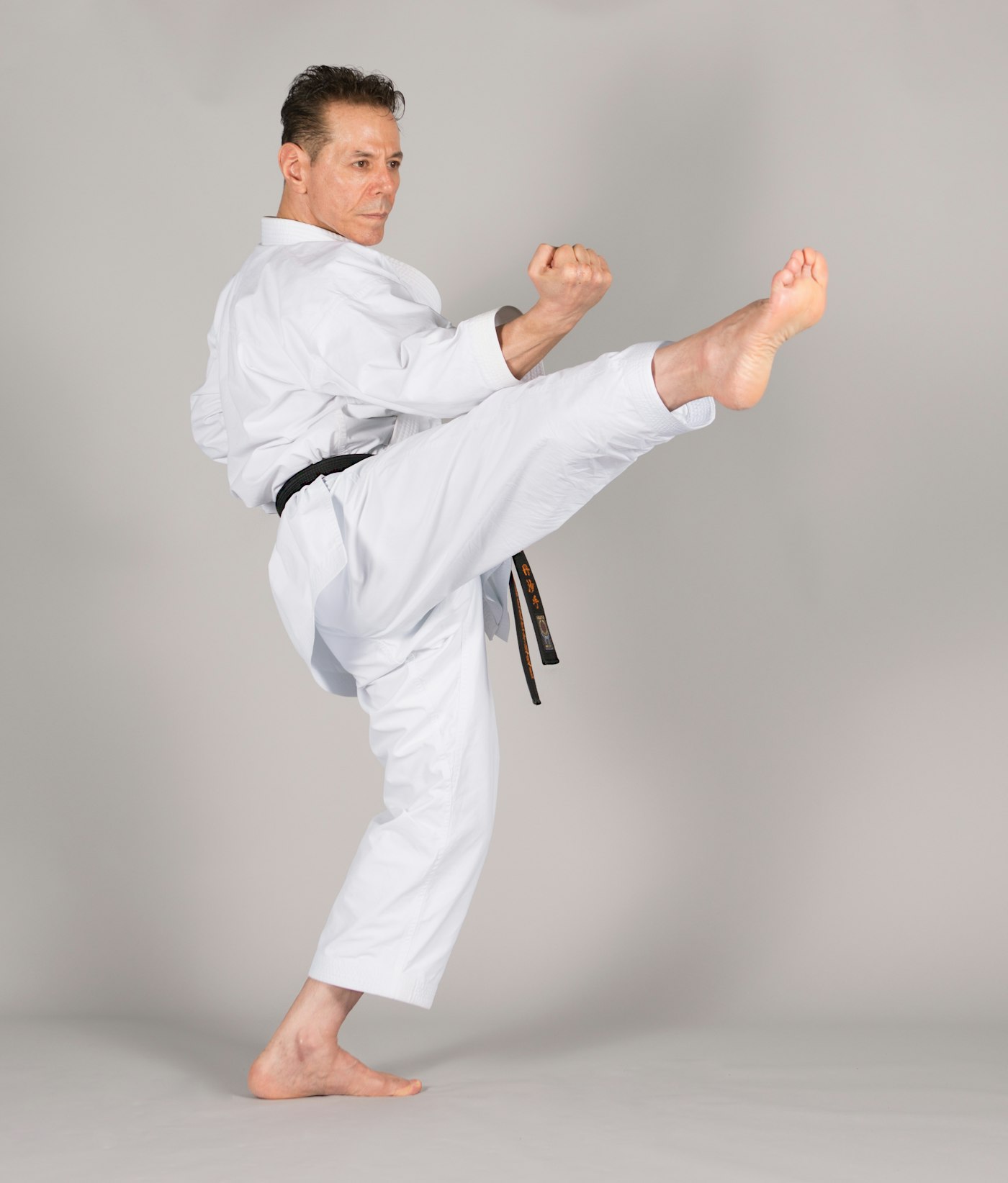 Karateka in a white gi throwing a high side kick against a plain grey background