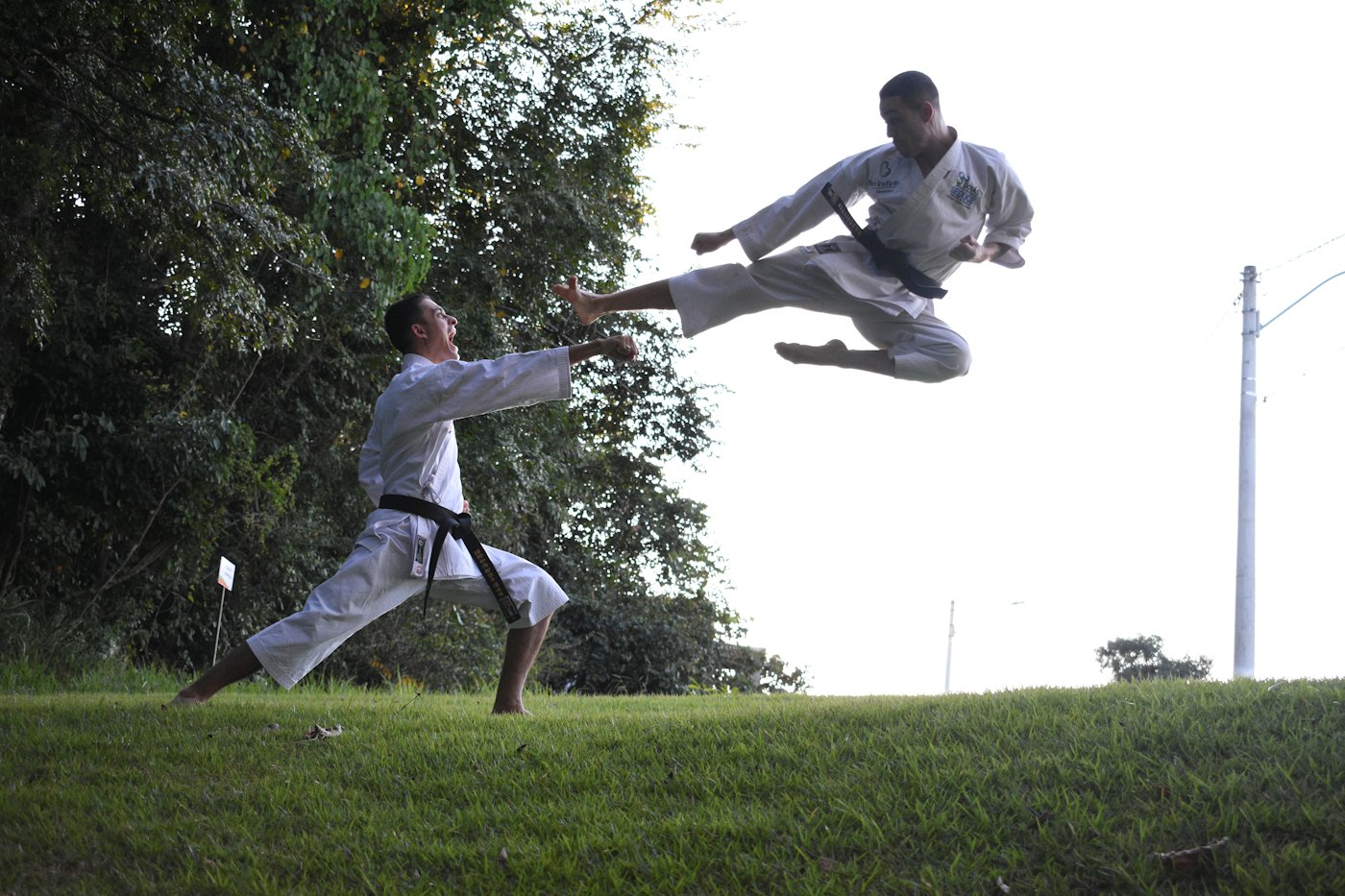 Two karateka sparring on grass, one leaping into a flying kick toward the other