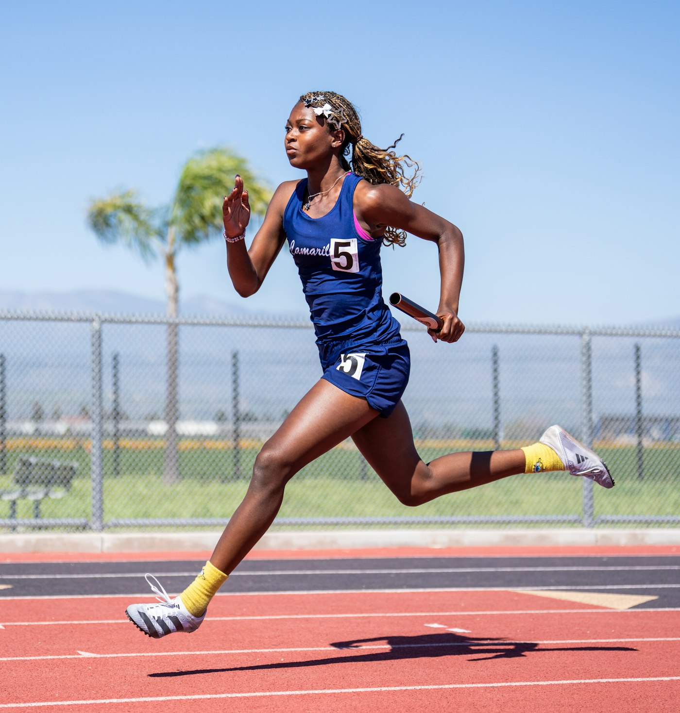 Female sprinter with a relay baton at full stride on a red track, seen from the side