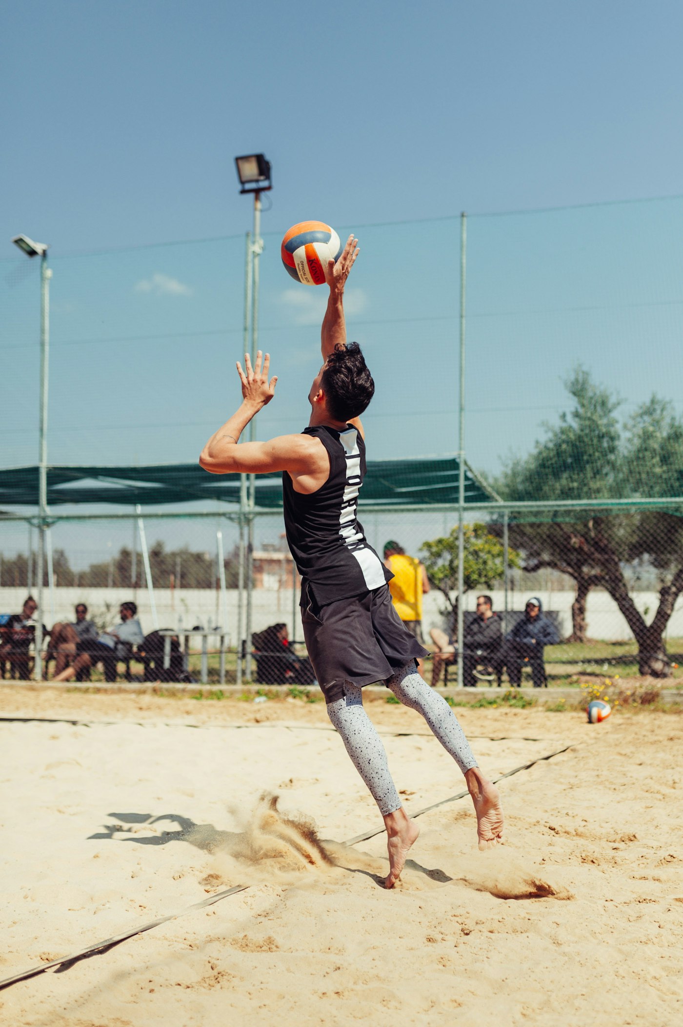 Beach volleyball player jumping and reaching overhead to hit the ball