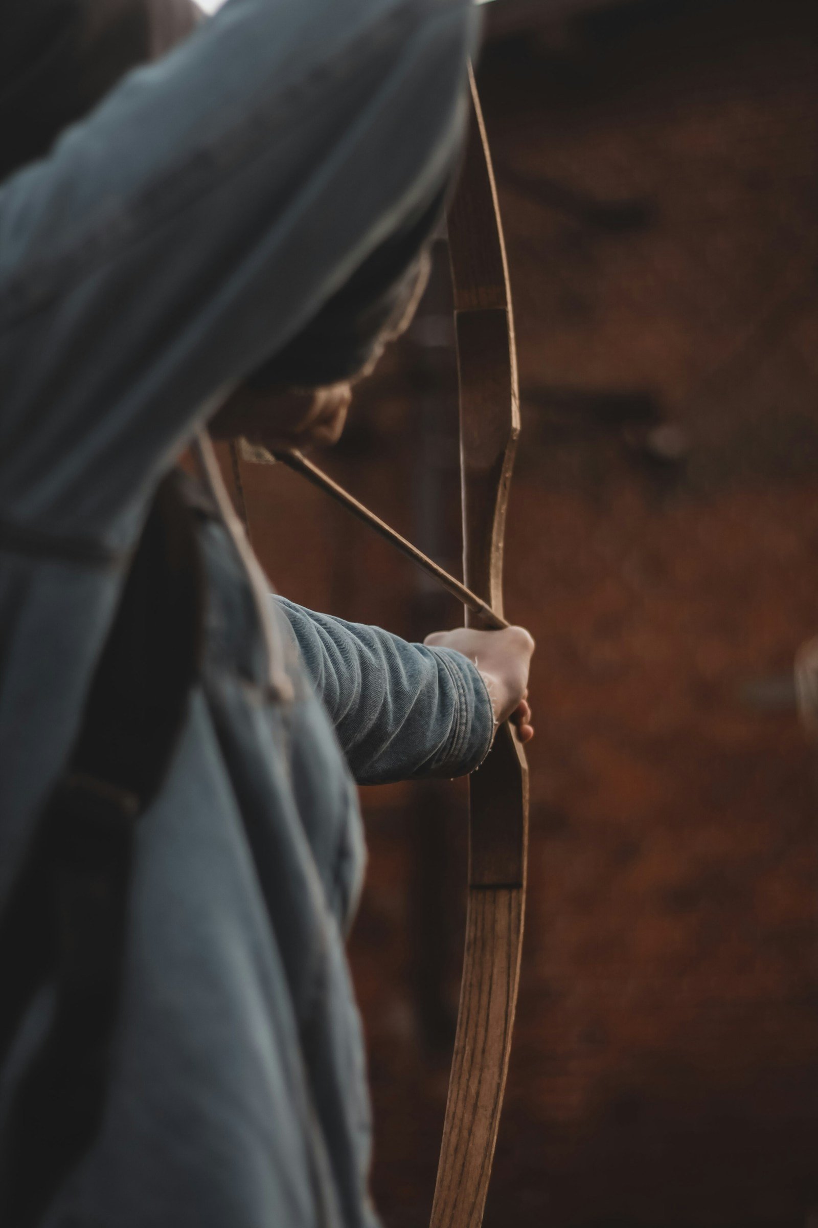 Close view of an archer drawing a wooden bow, the hand at the string and the bent bow limb