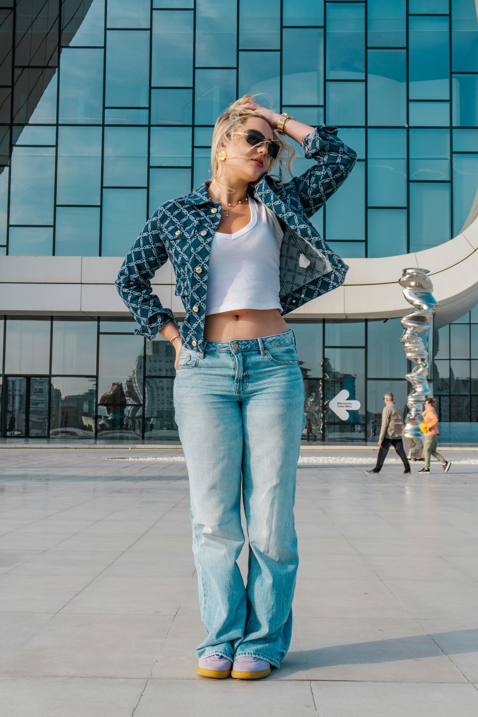 Woman in a denim jacket, white top and jeans standing outside a modern building