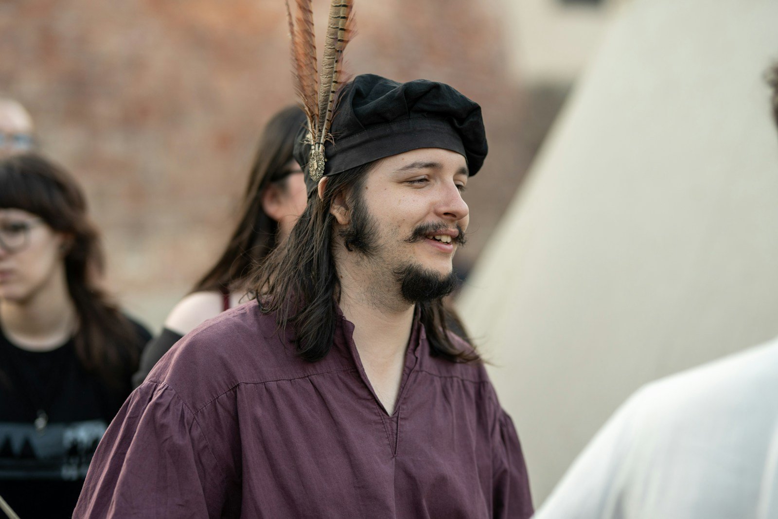 Man in a purple tunic and a black hat with a feather at a medieval fair