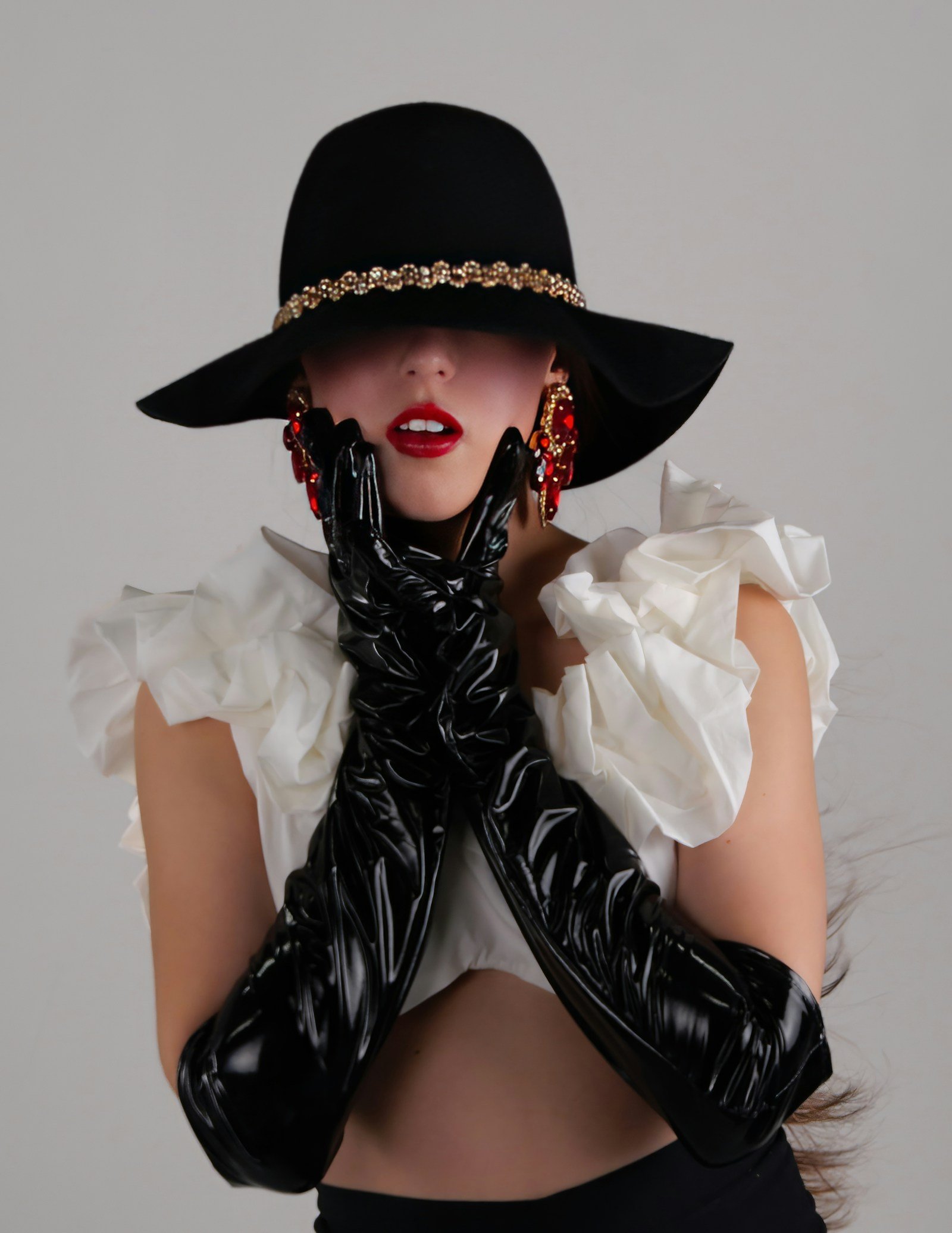 Woman in a wide-brim black hat and long black gloves with her hands raised to her face