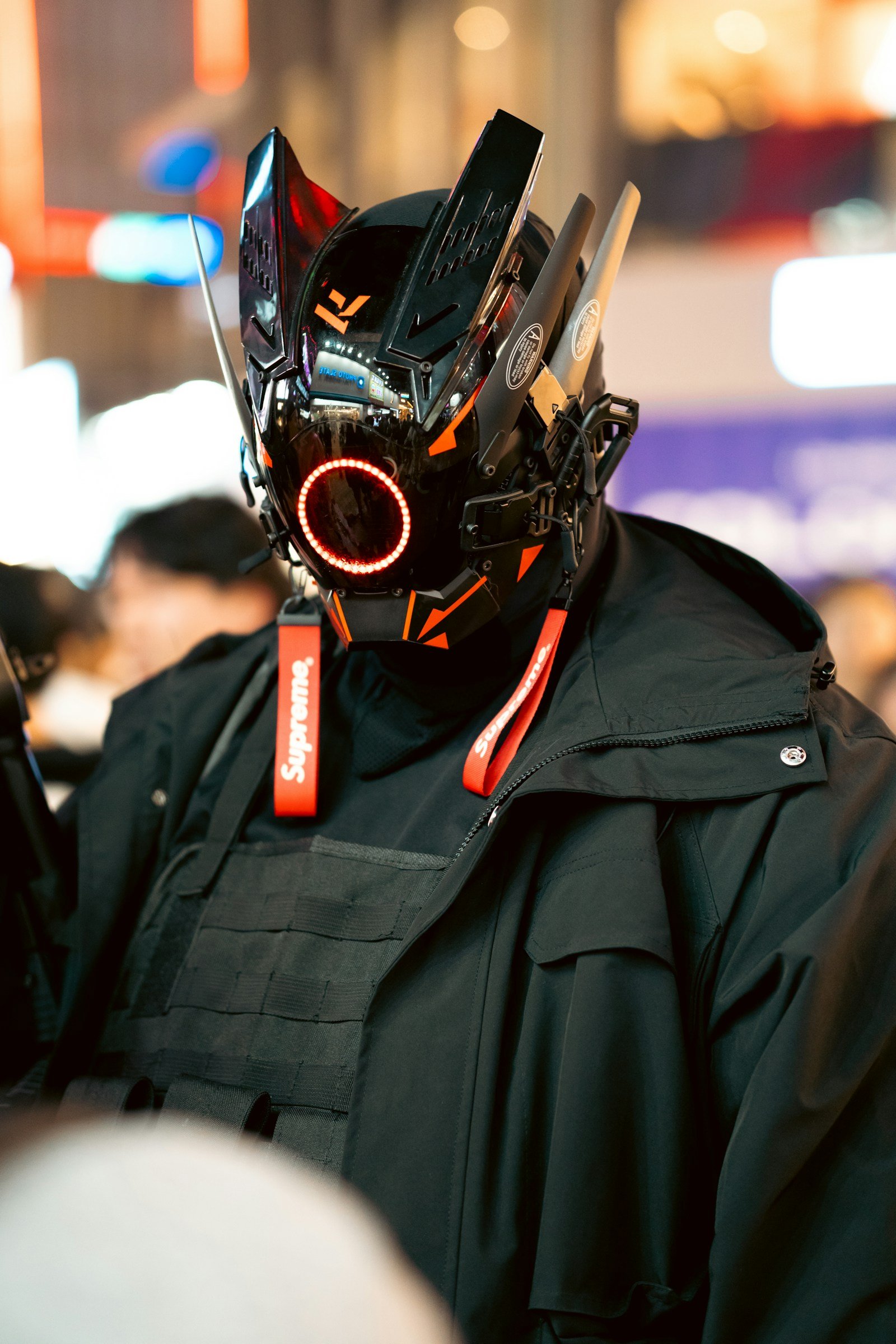 Man in dark clothing and a mask with electronic gadgets and red cables attached