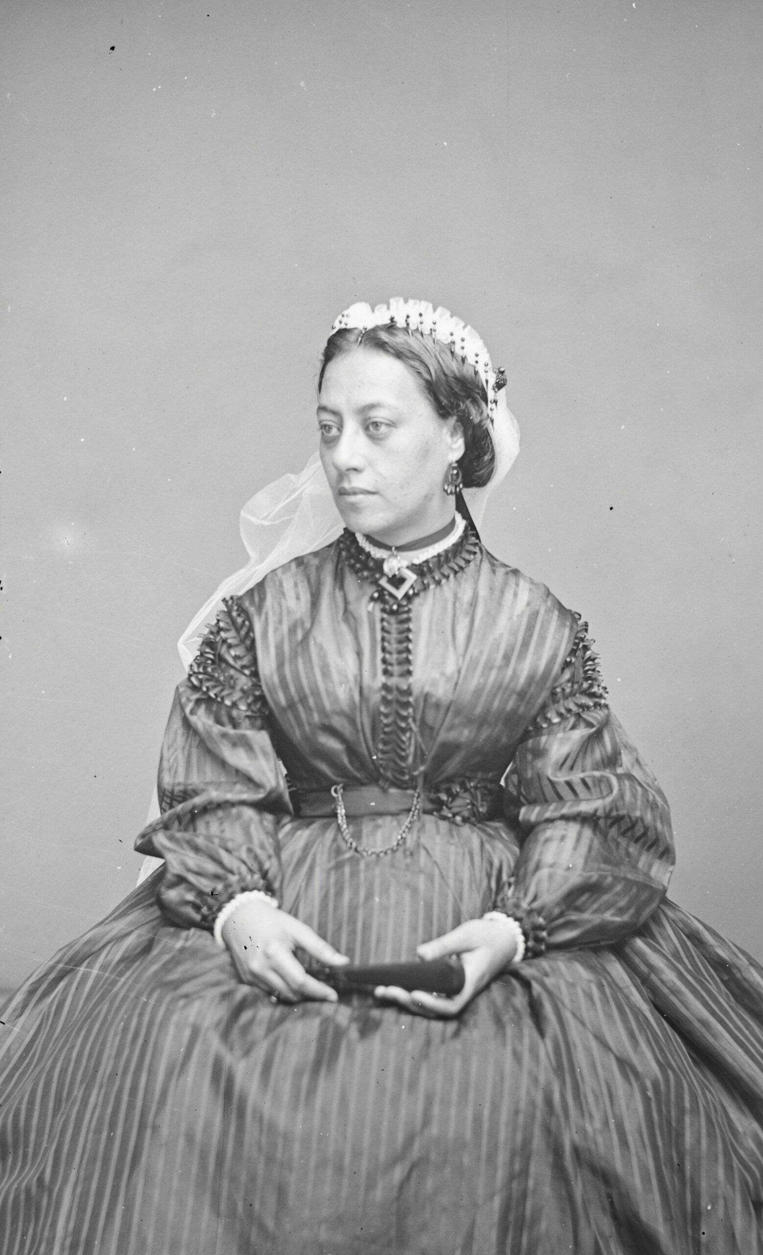 Black and white portrait of a seated woman in a striped Victorian dress with a lace headpiece