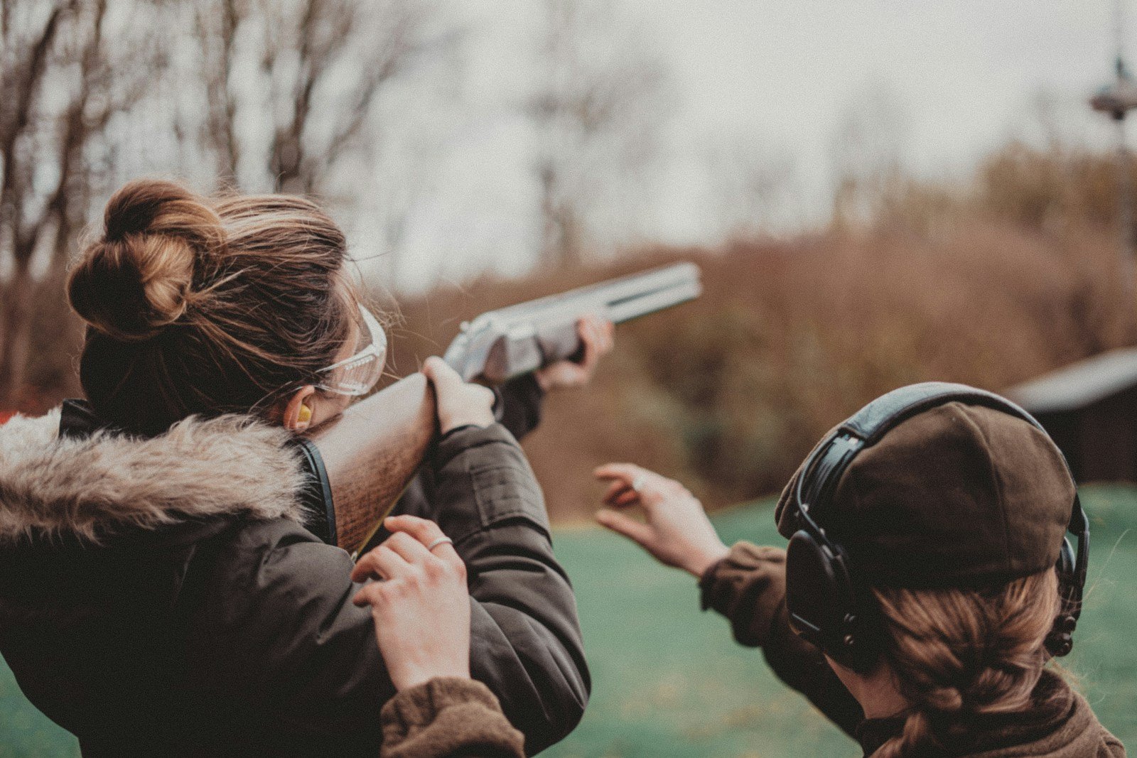Woman shouldering a shotgun at a shooting range with an instructor beside her