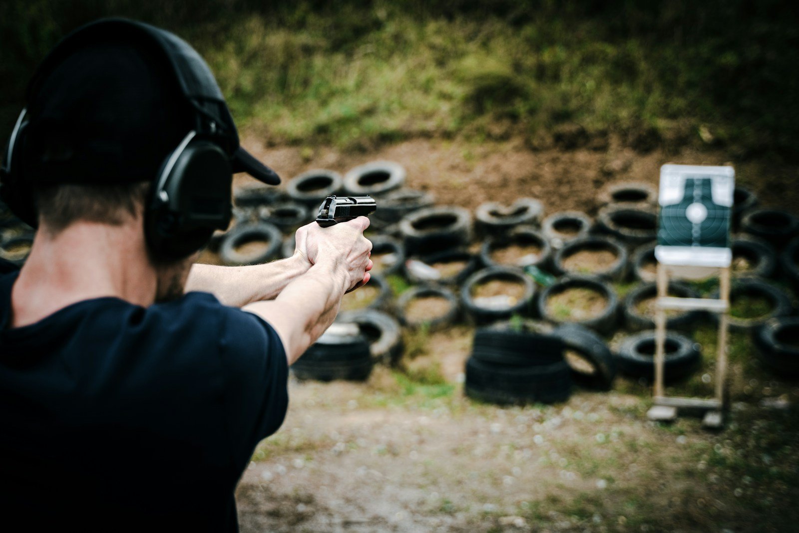 Man in ear protection aiming a pistol with both hands at a target on a shooting range