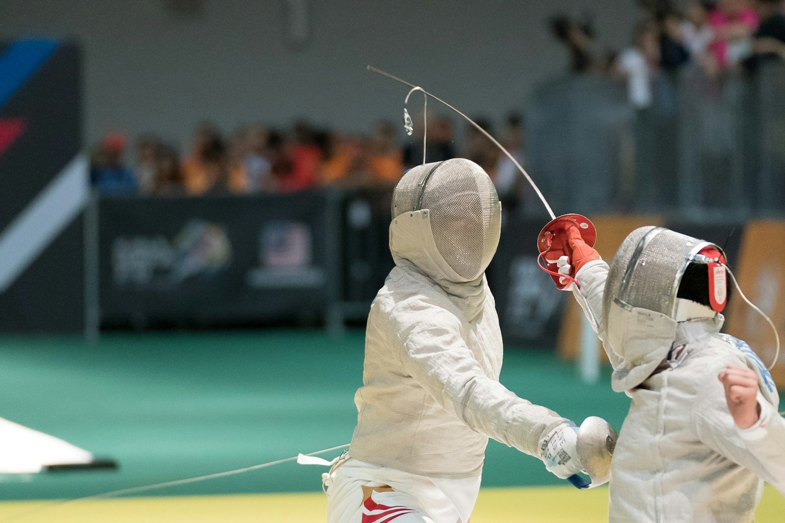 Two fencers in white lunging at each other during a match, weapon arms extended