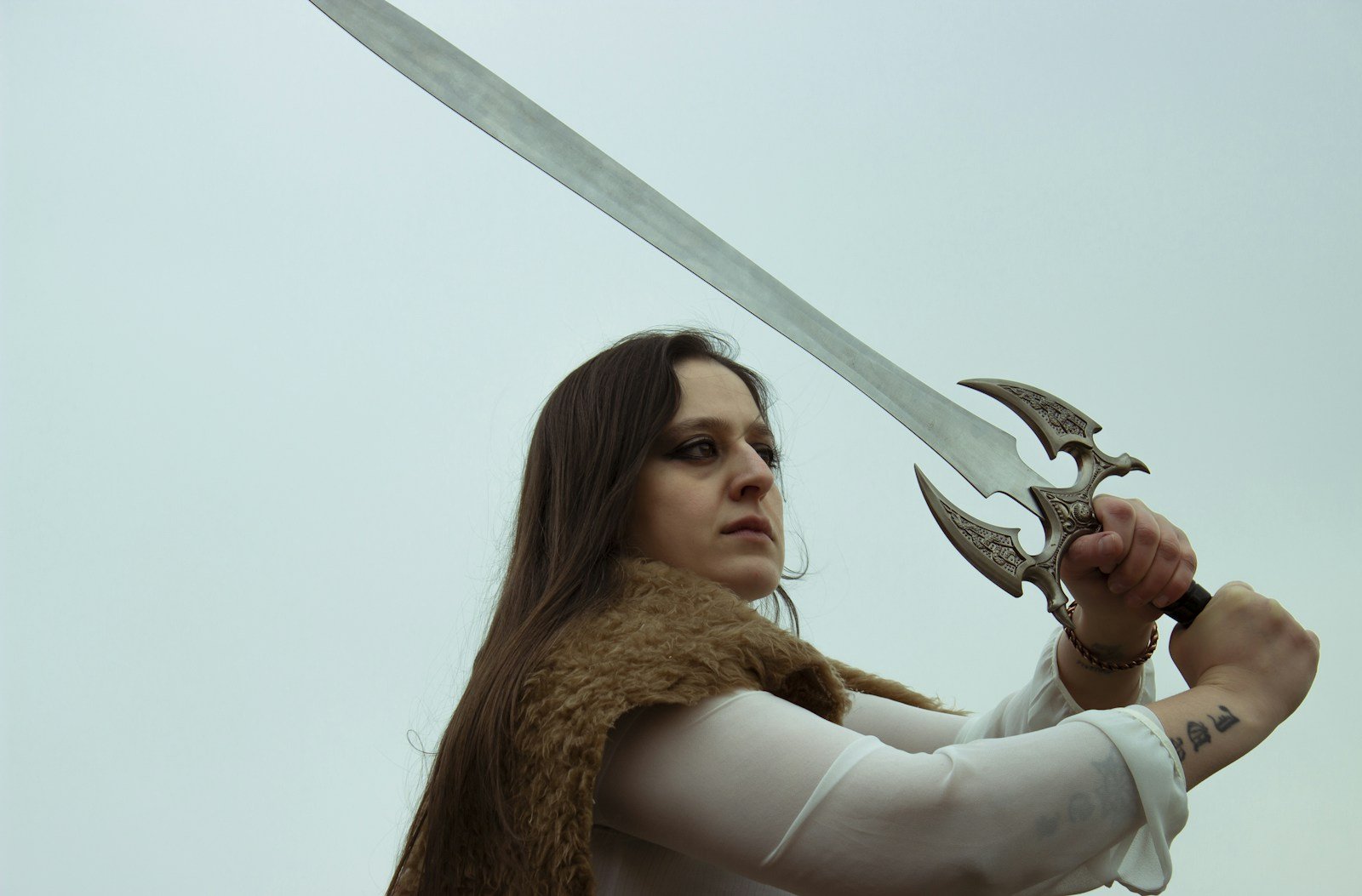 Woman holding a long sword up in a two-handed guard, a weapon pose reference for sword poses
